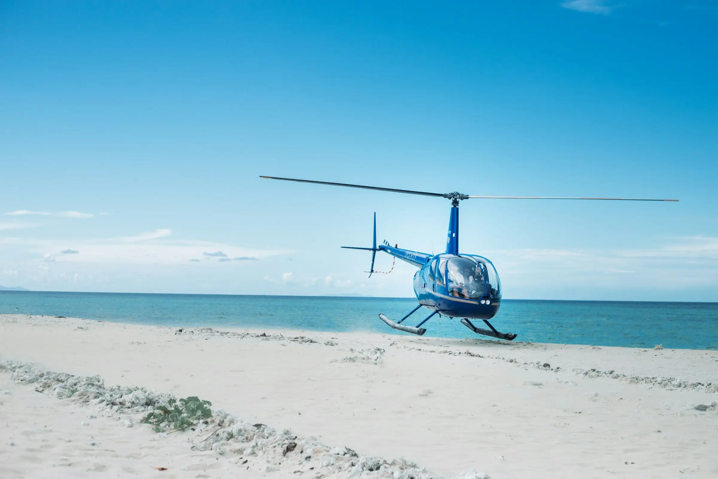 Hélicoptère posé sur une plage de sable blanc, au bord de l’océan